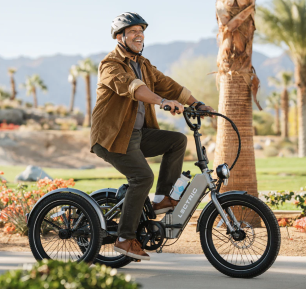 Smiling man on an electric tricycle wearing a bike helmet.